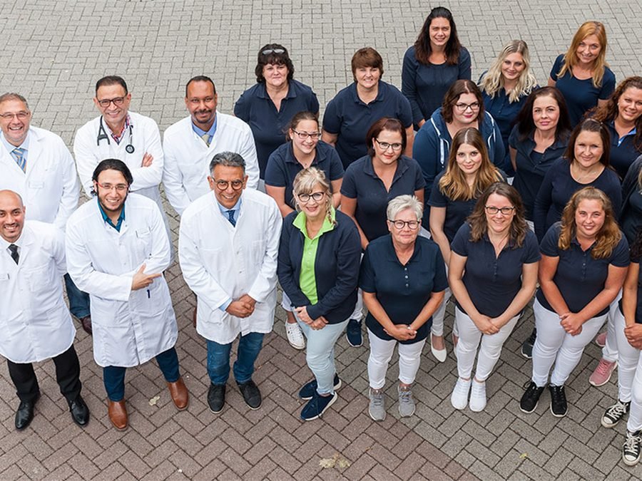Gruppenbild des Praxisteams in dunkelblauer Dienstkleidung und weißen Arztkitteln